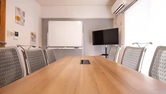 会議テーブルと6脚のオフィスチェア。奥にホワイトボードとモニター